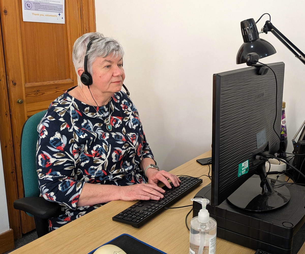 A staff member at the Down to Earth funeral poverty service sitting at their computer at their desk, wearing a headset and typing.
