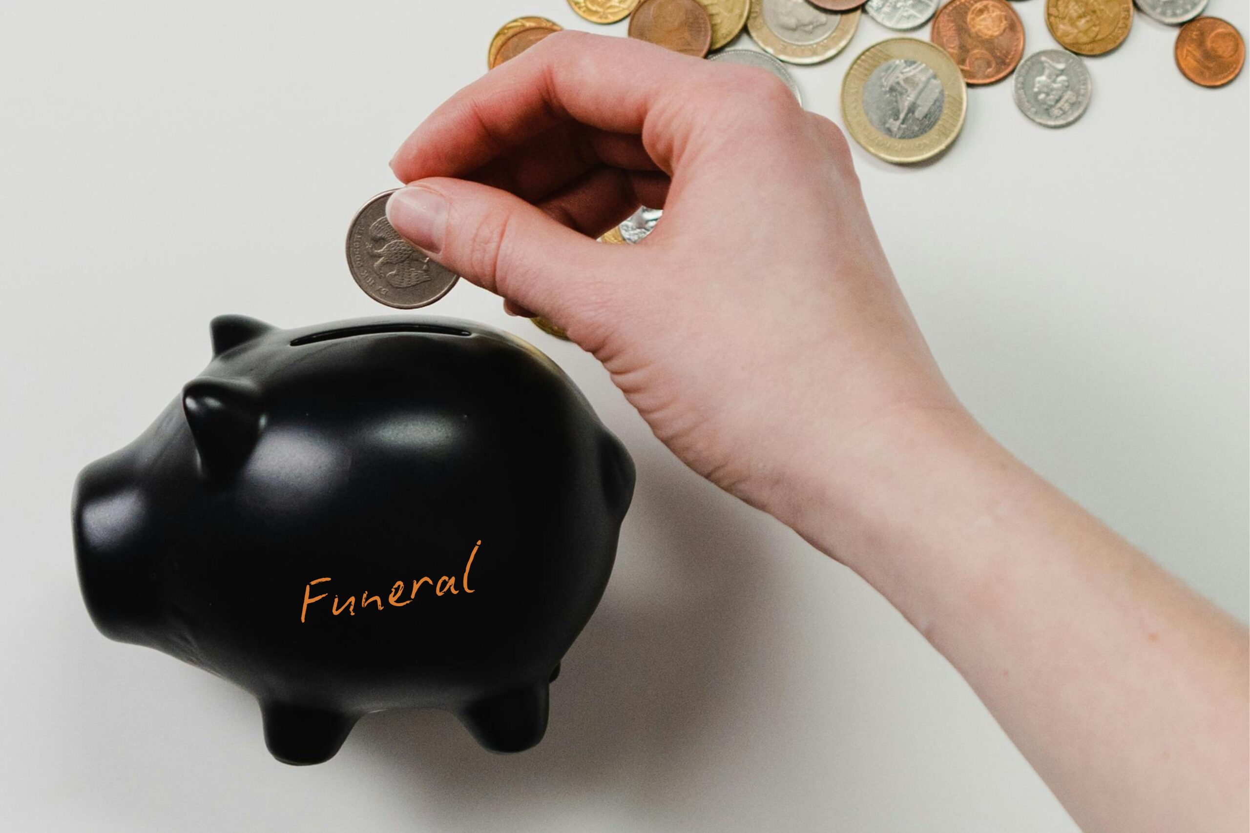 Black piggy bank with the word funeral written on it. A white person's hand is putting a coin into the top.