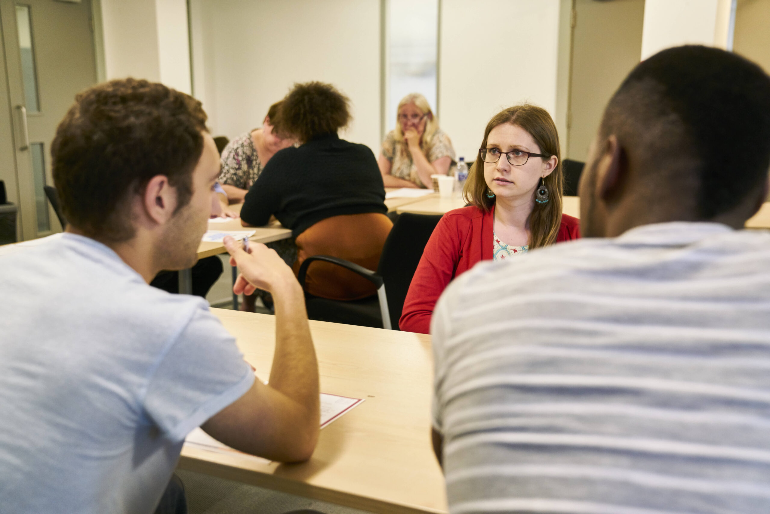 A black man, a white man and a white woman are sat at a table in a large room. There are other people in the background.