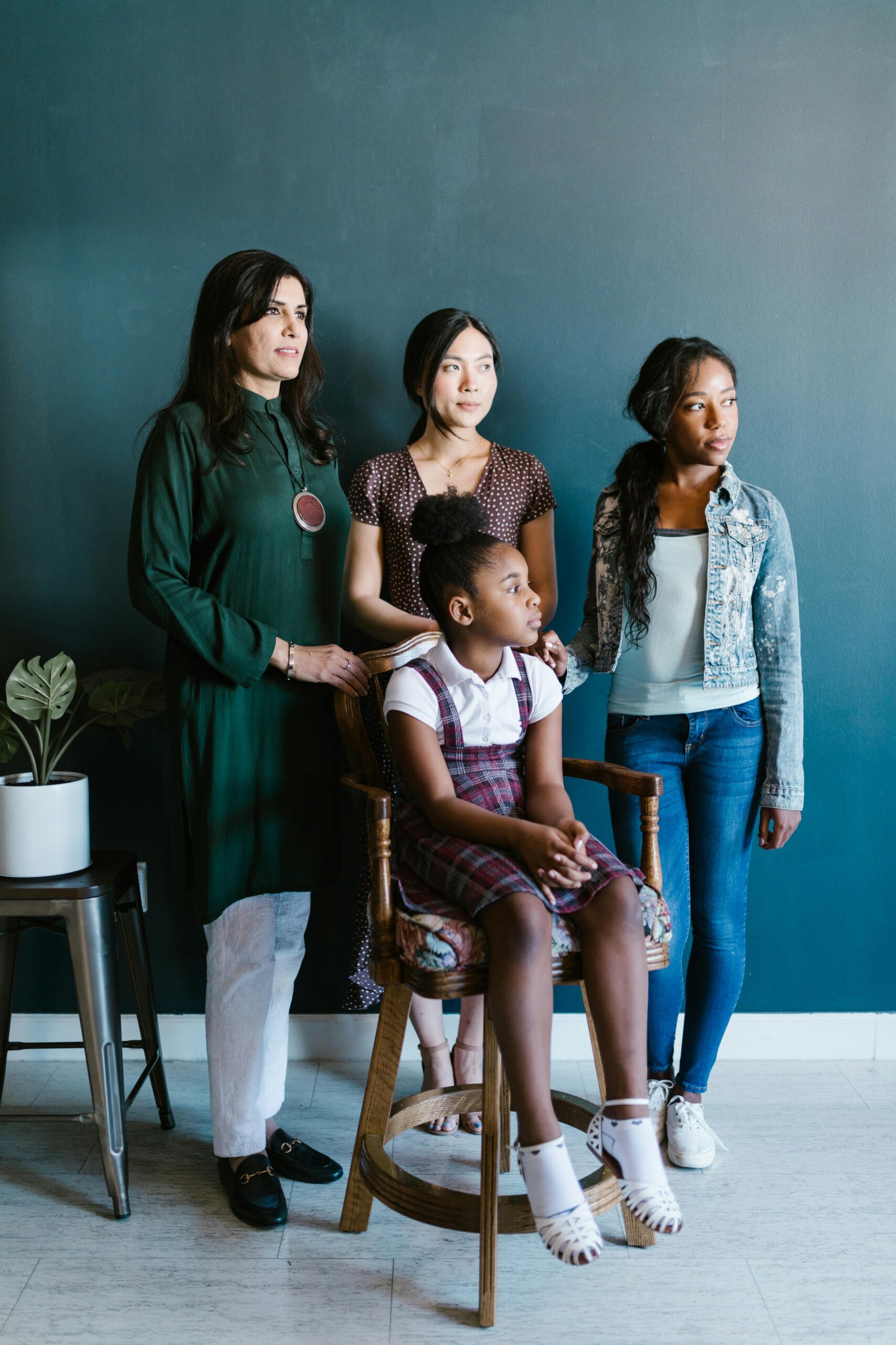 One Asian woman is stood with two Asian female adolescents behind a seated Asian adolescent female.