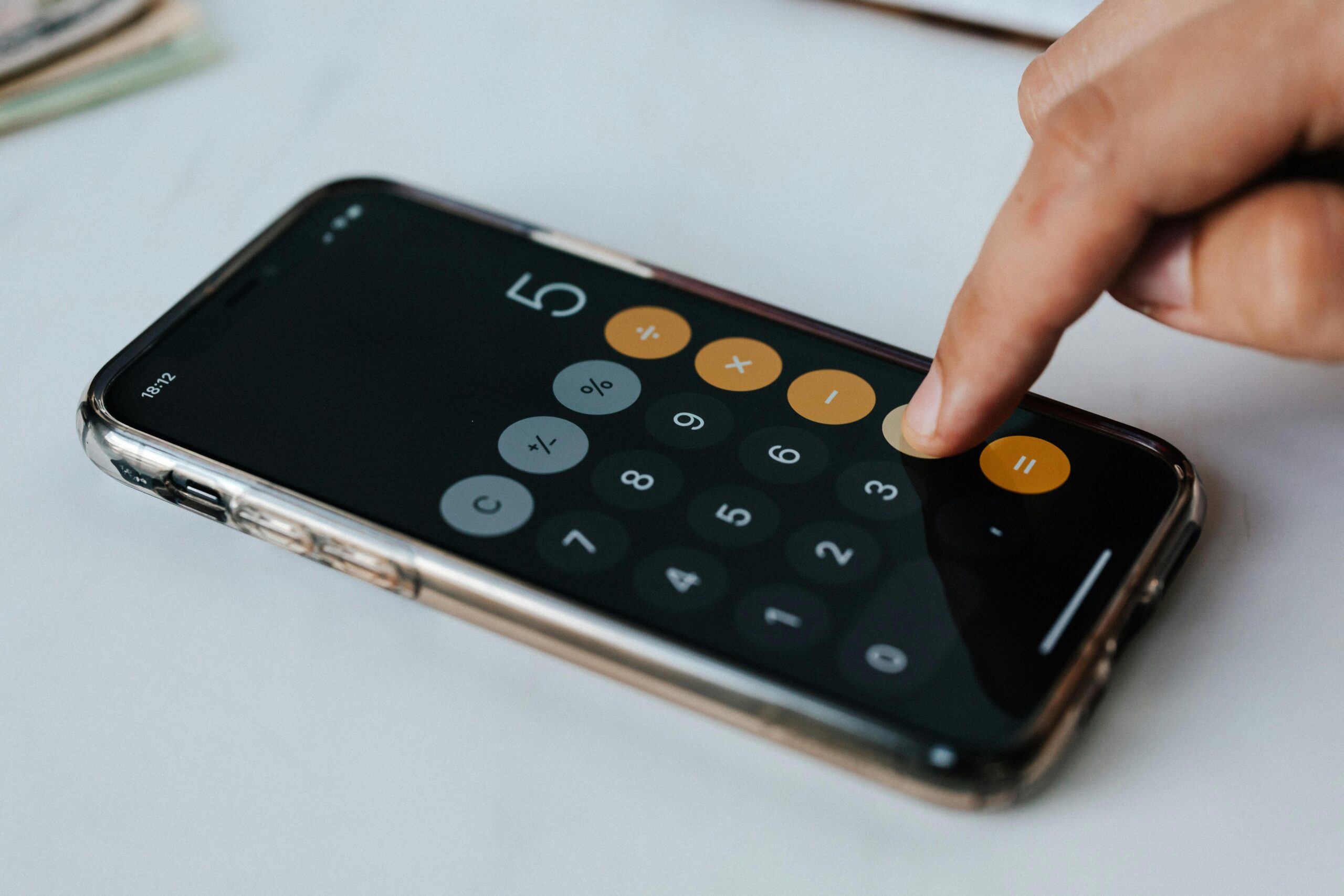 A calculator open on a mobile phone. A white person's finger is pressing a button on it.