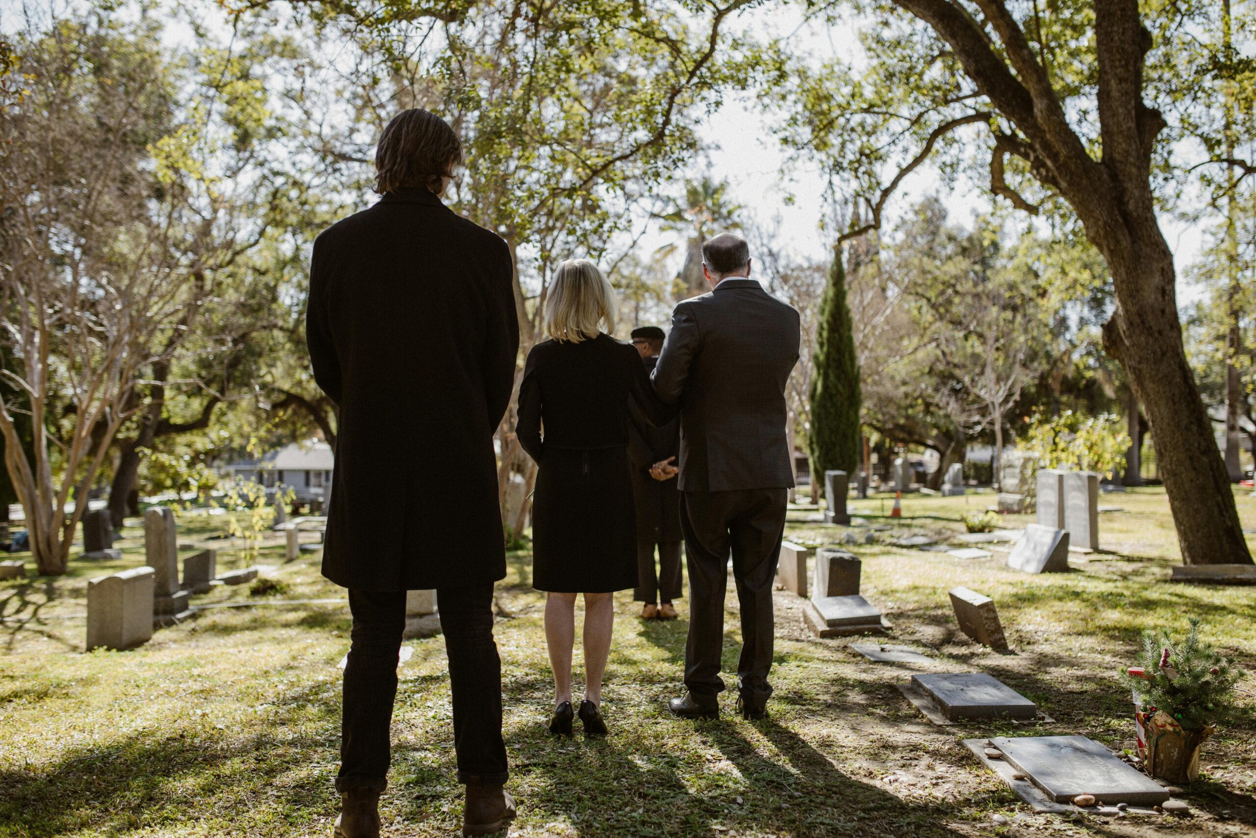 A group of people are standing in a cemetery with their backs to the camera.
