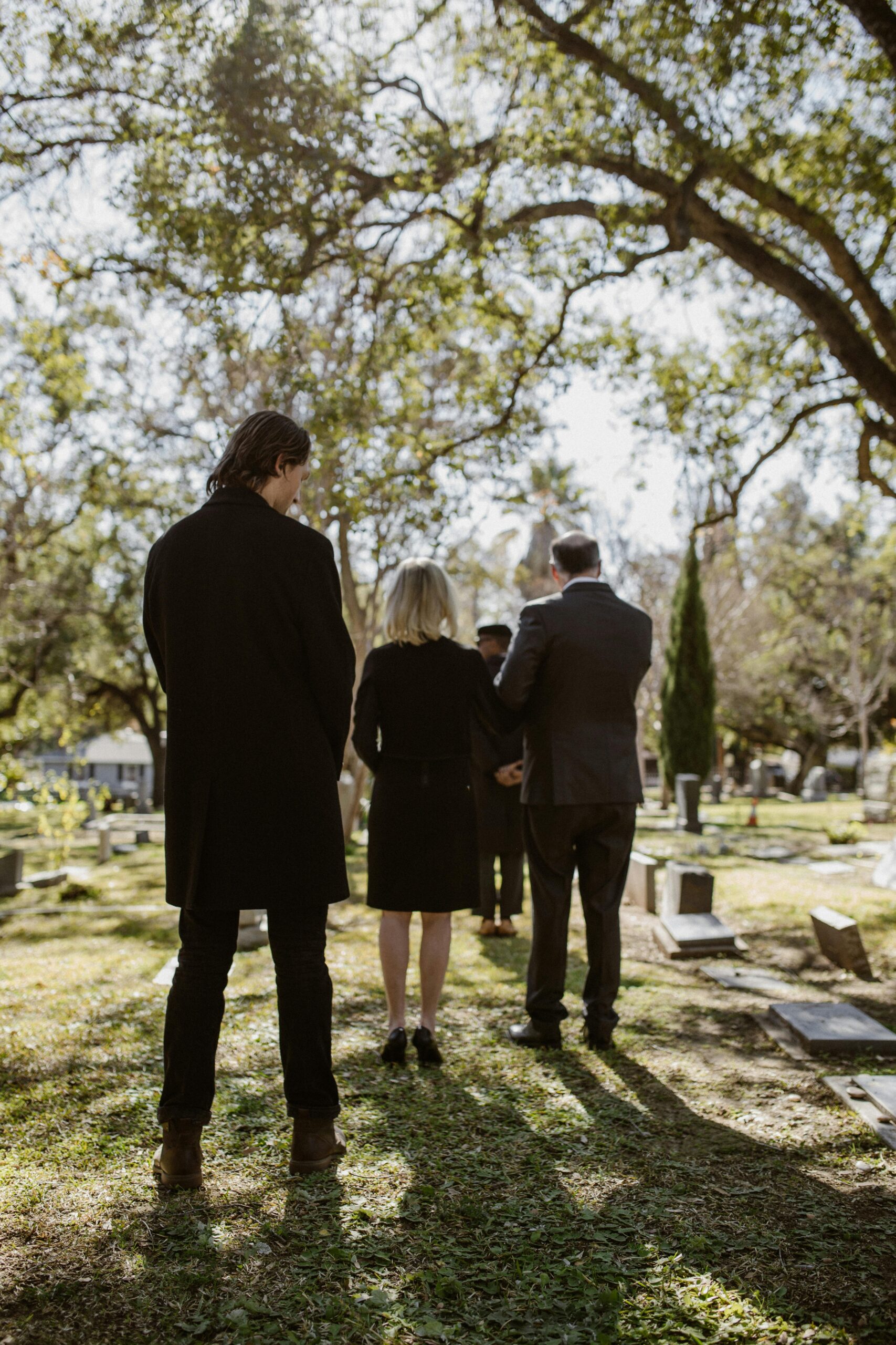 A group of people are standing in a cemetery with their backs to the camera.