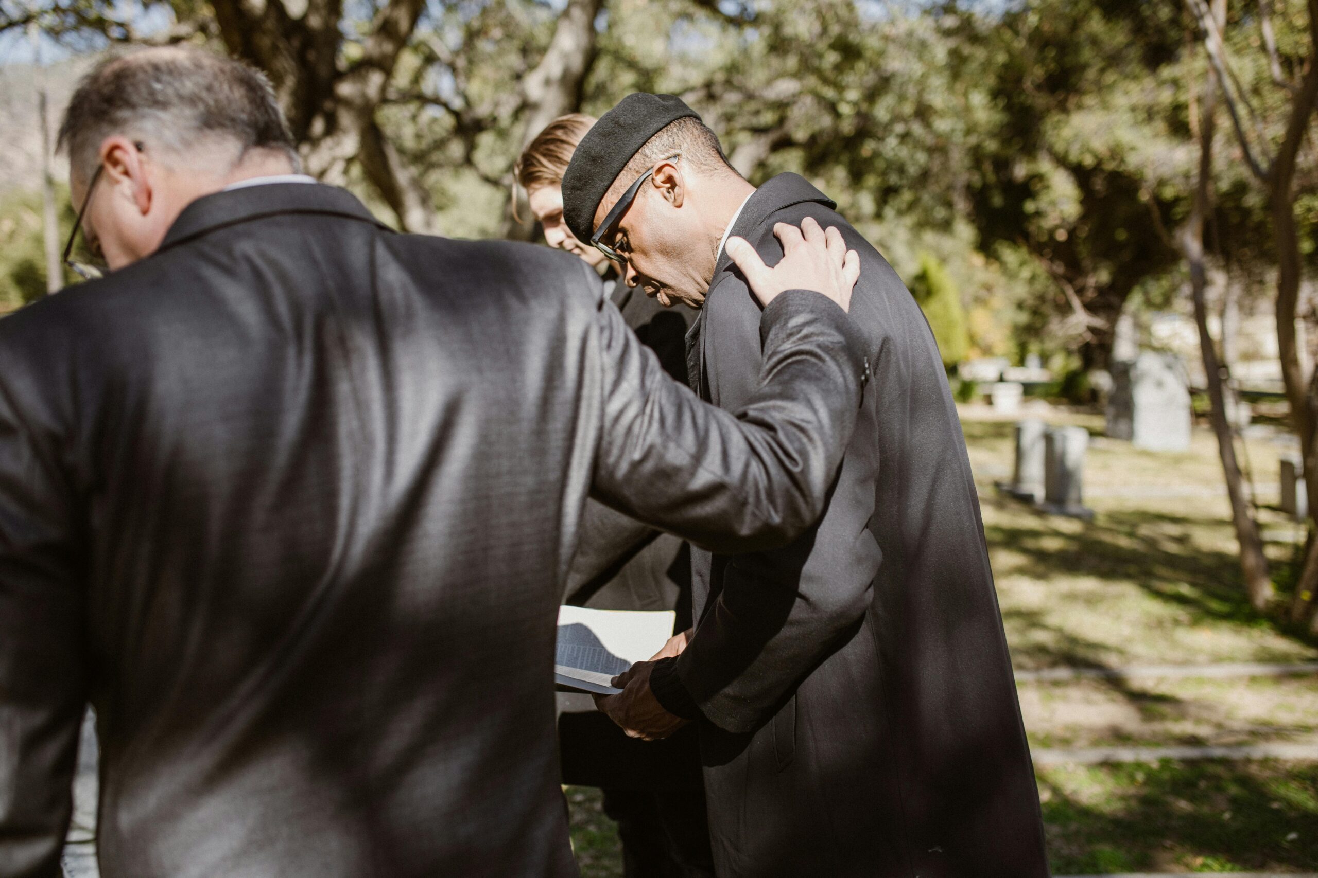 A black man and a white man are standing outside. The black man is reading from a book. The white man has his hand on the black man's shoulder.