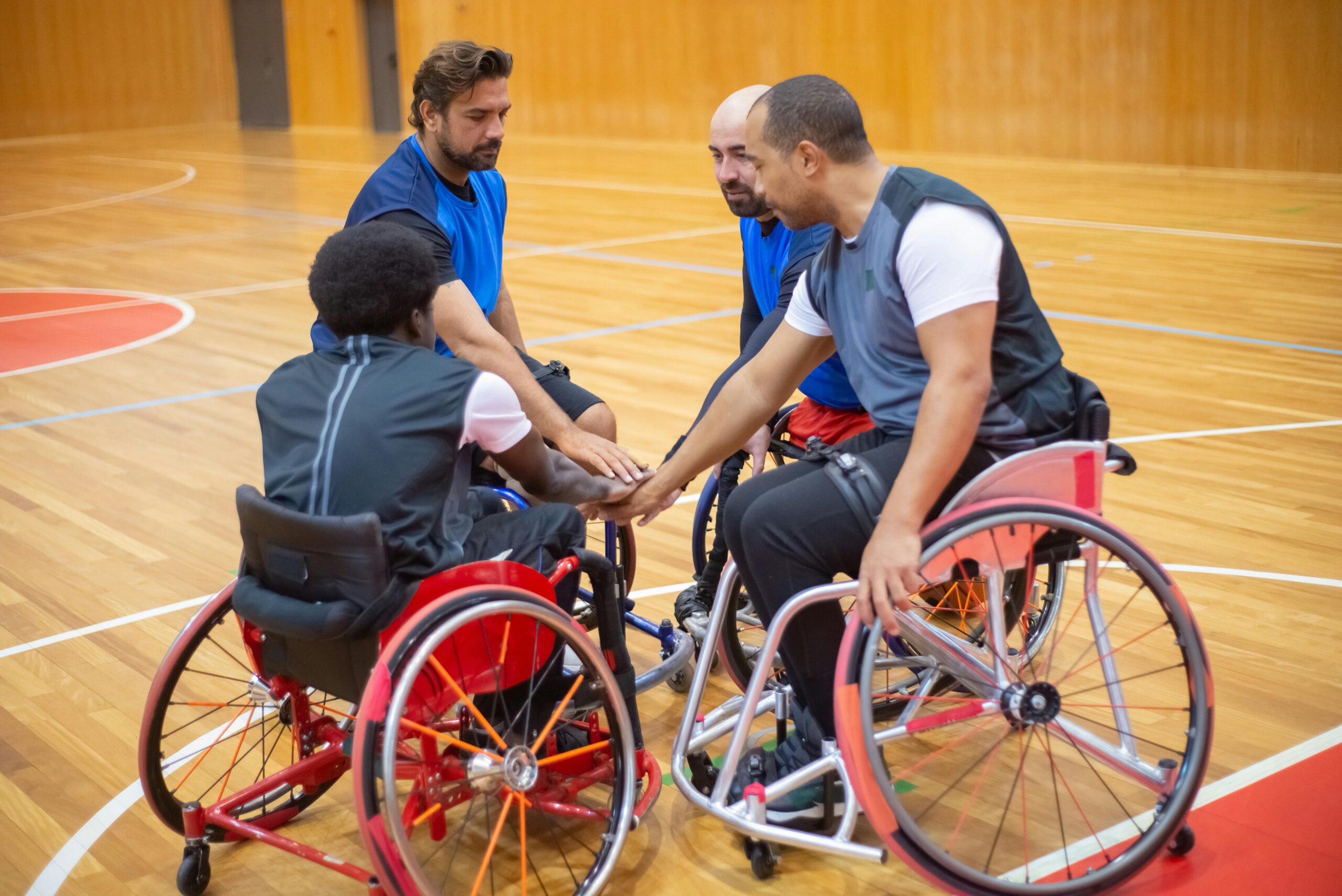 Four members of a male wheelchair basketball team are in a huddle with their hands in the middle of the circle.